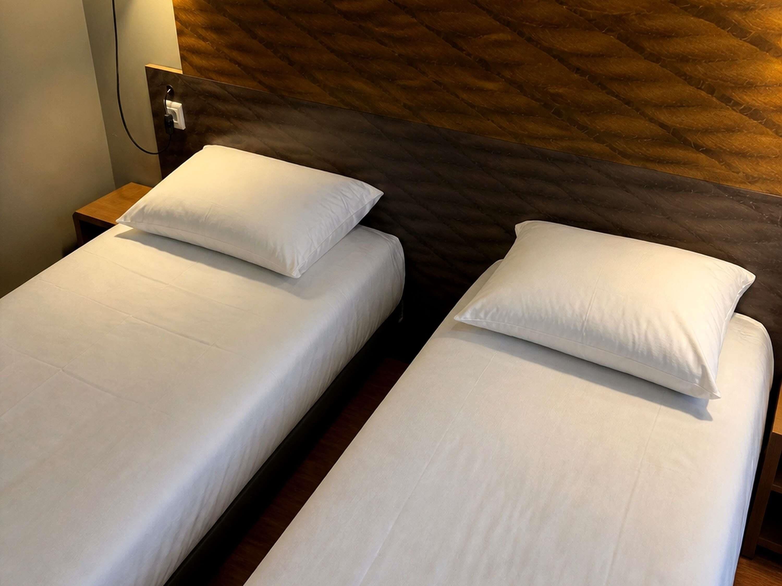 Dos camas individuales con ropa de cama blanca en una habitación con cabecera de madera y mesita de noche.