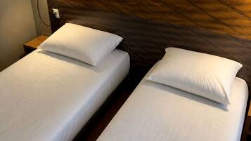 Dos camas individuales con ropa de cama blanca en una habitación con cabecera de madera y mesita de noche.