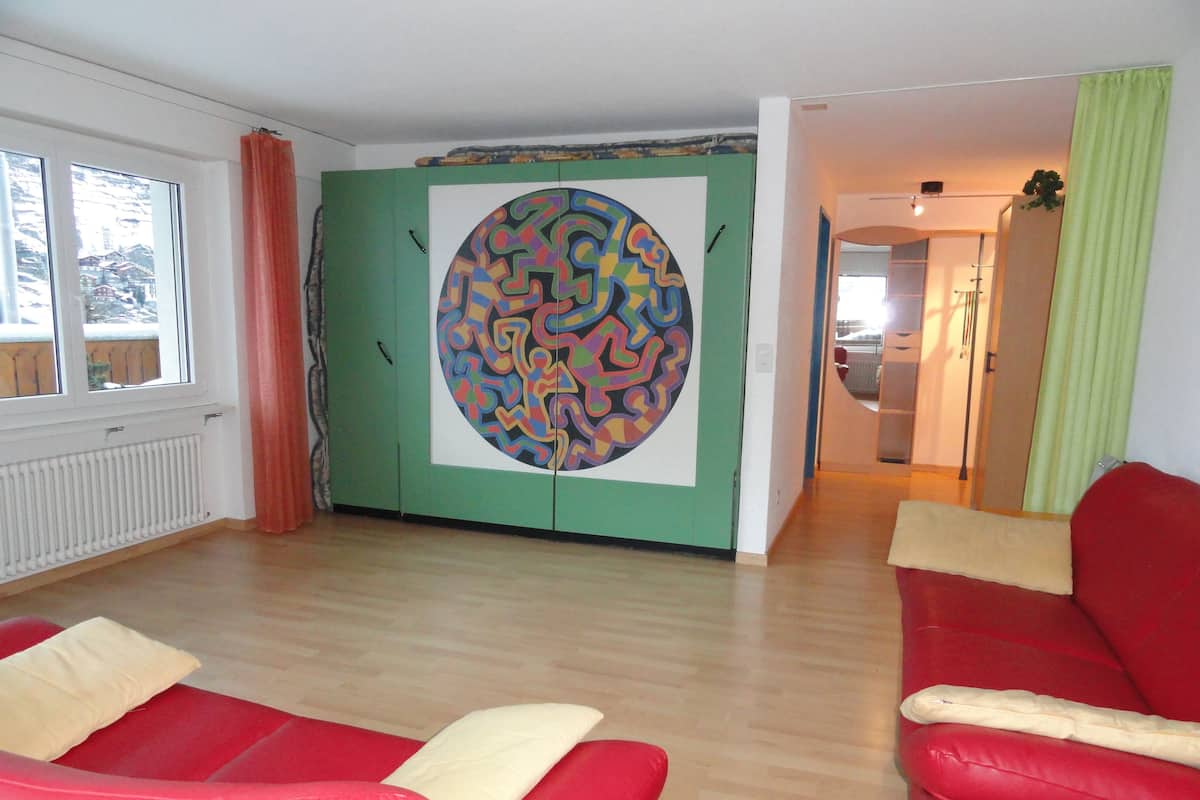 A living room with a red sofa, a green cabinet with a colorful circular design, and a view of a snowy landscape through a window.