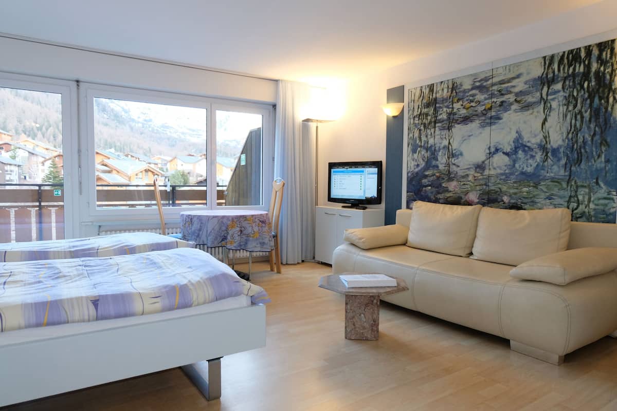 A hotel room with a bed, a sofa, a TV, and a painting.