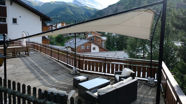 A balcony with outdoor furniture, a wooden fence, and a view of a mountain with a snow-capped peak. - Artist Apartments & Hotel Garni (Zermatt)