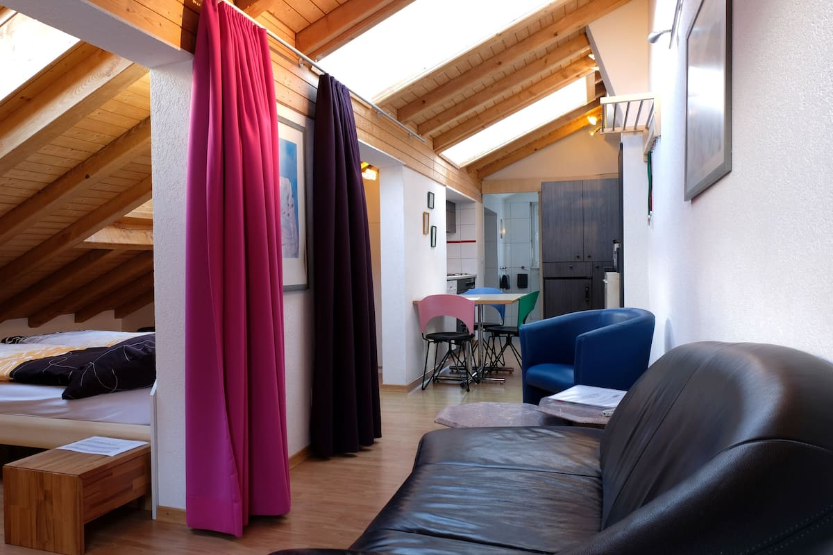 A cozy loft bedroom with a sloped ceiling, a bed, a wooden bench, and a dining area with a table and chairs.