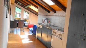 A kitchen with wooden beams, a dining area with chairs, and a view through a window. - Artist Apartments & Hotel Garni (Zermatt)