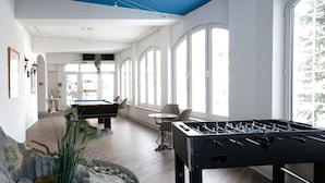 A spacious indoor area with a foosball table, a pool table, and large windows allowing natural light. - Artist Apartments & Hotel Garni (Zermatt)