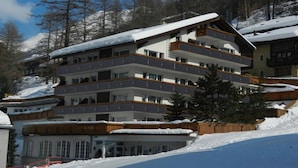 A multi-story hotel with balconies, surrounded by snow-covered trees and mountains. - Artist Apartments & Hotel Garni (Zermatt)
