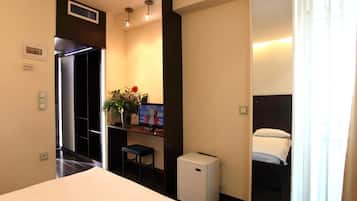 A hotel room with a bed, a small desk with a computer, a refrigerator, and a window with curtains.