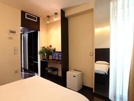 Una habitación de hotel con cama, un escritorio pequeño con computadora, refrigerador y ventana con cortinas.