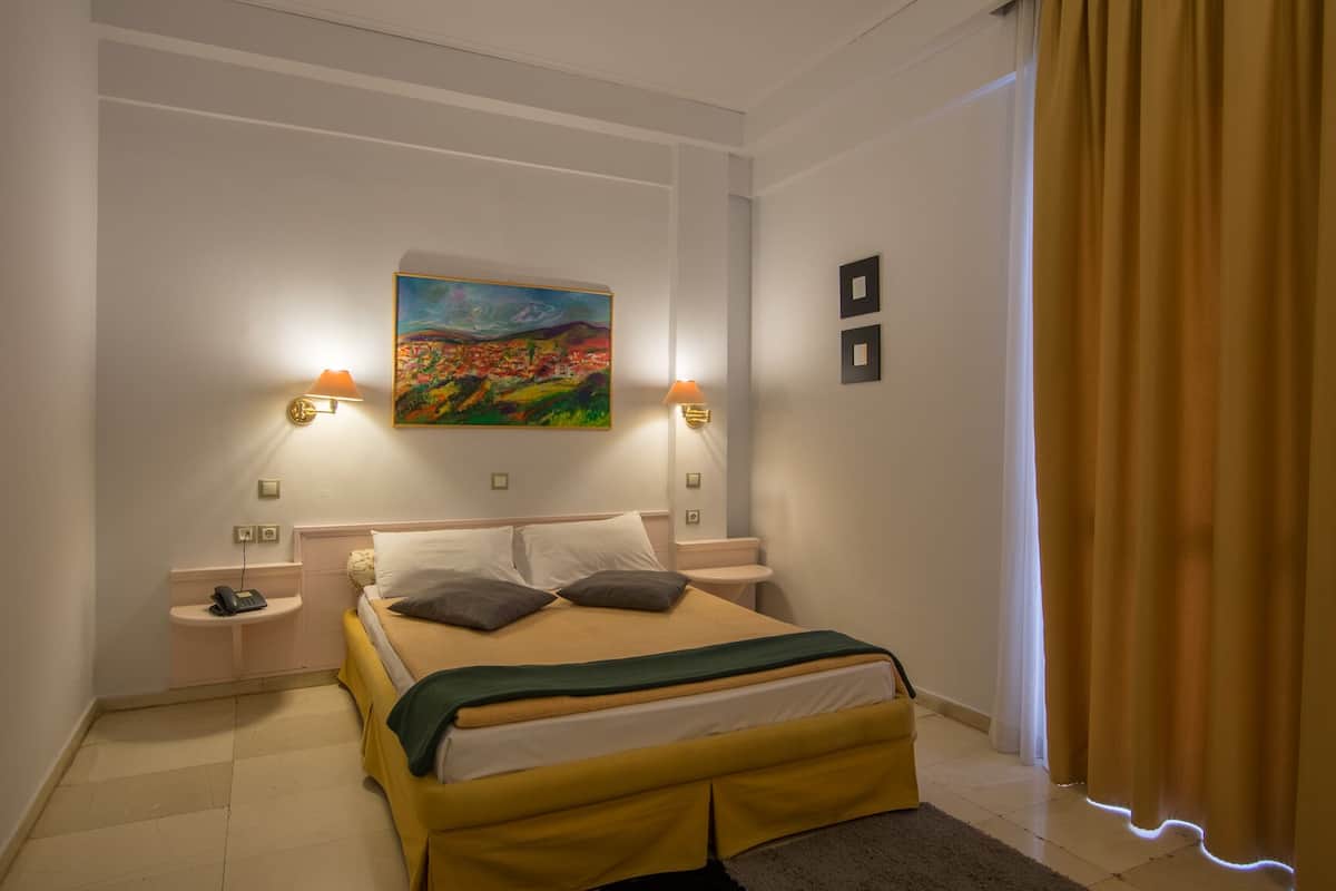 A hotel room with a bed, bedside lamps, a painting on the wall, and a curtain.