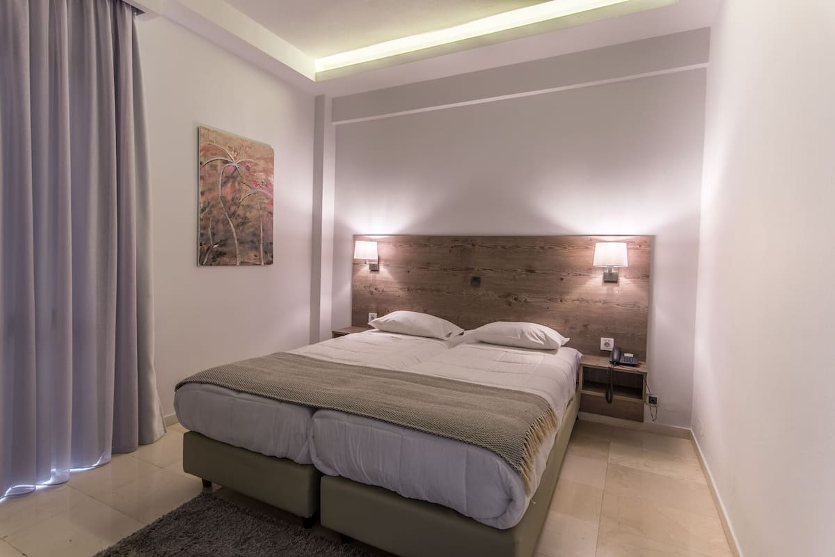 A modern bedroom with a large bed, two bedside tables with lamps, a painting on the wall, and a grey curtain.