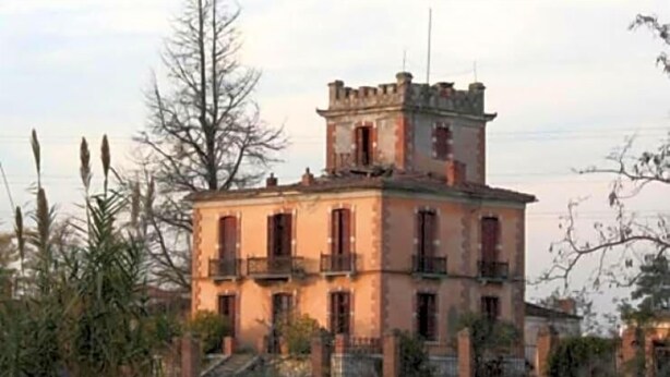 Un edificio histórico con una torre central, múltiples ventanas y fachada de piedra.