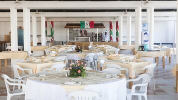 Une salle de réception avec des tables rondes et des chaises blanches, un espace dédié aux plats de pâtes et un buffet.