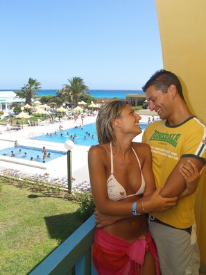 A couple on a balcony overlooking a pool area with a view of the ocean. - El Mouradi Cap Mahdia (Mahdia)
