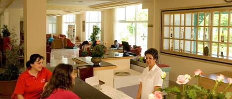 A hotel reception area with a counter, a clock, and a large window with a view of the outdoors.