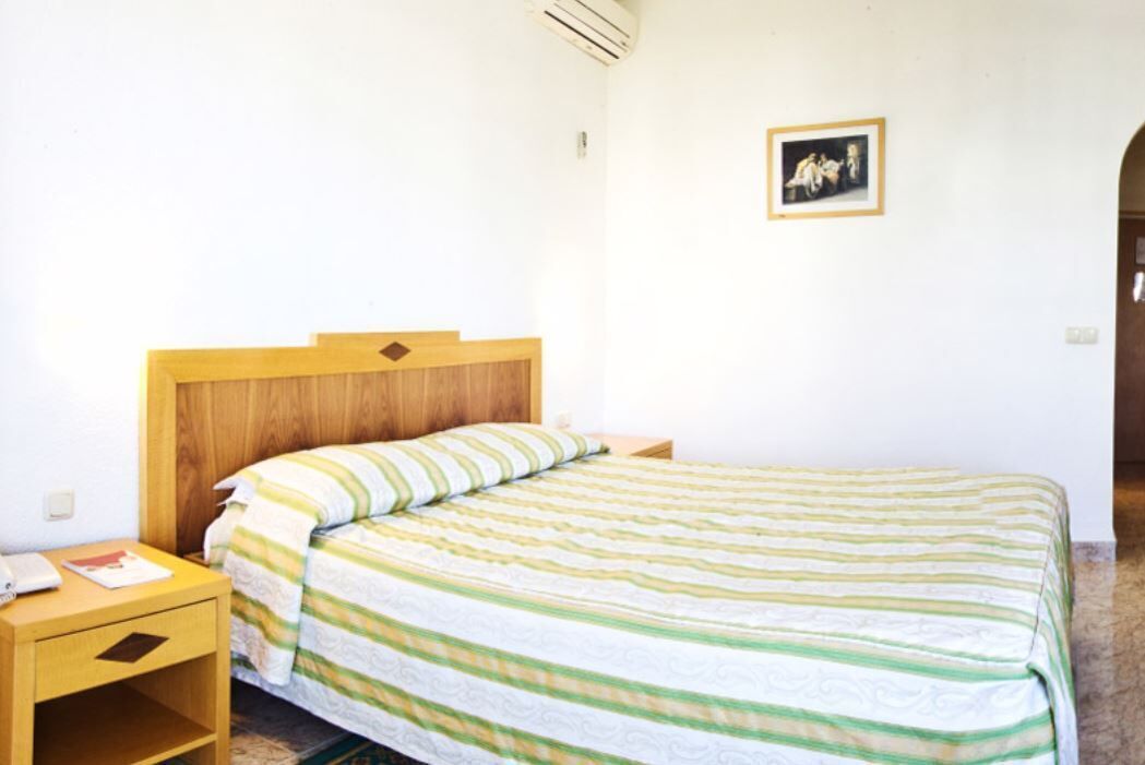 A single bed with a wooden headboard, a bedside table with a lamp, and a framed picture on the wall.