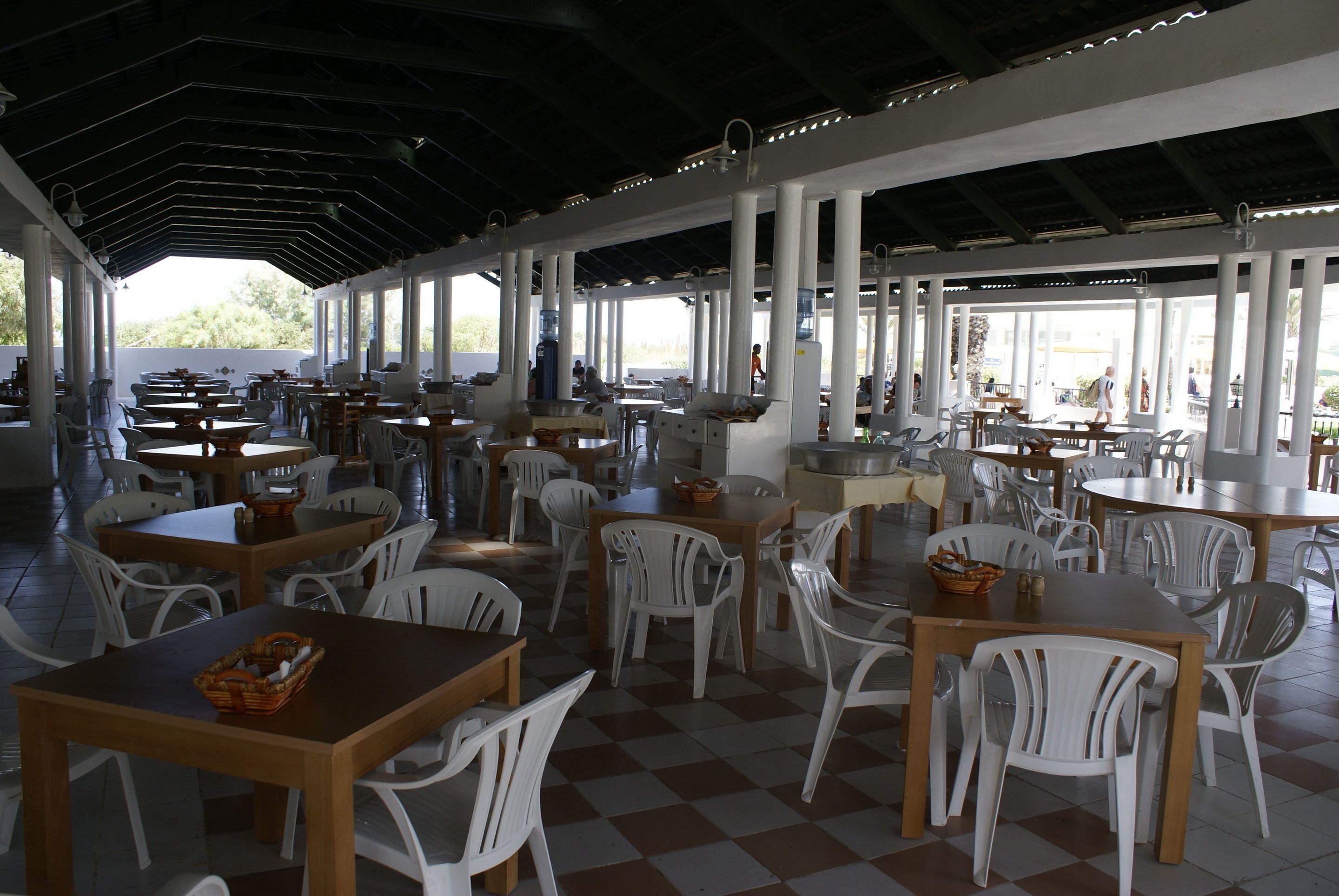 Un espacio de comedor al aire libre con mesas y sillas, techo cubierto y vistas del exterior.