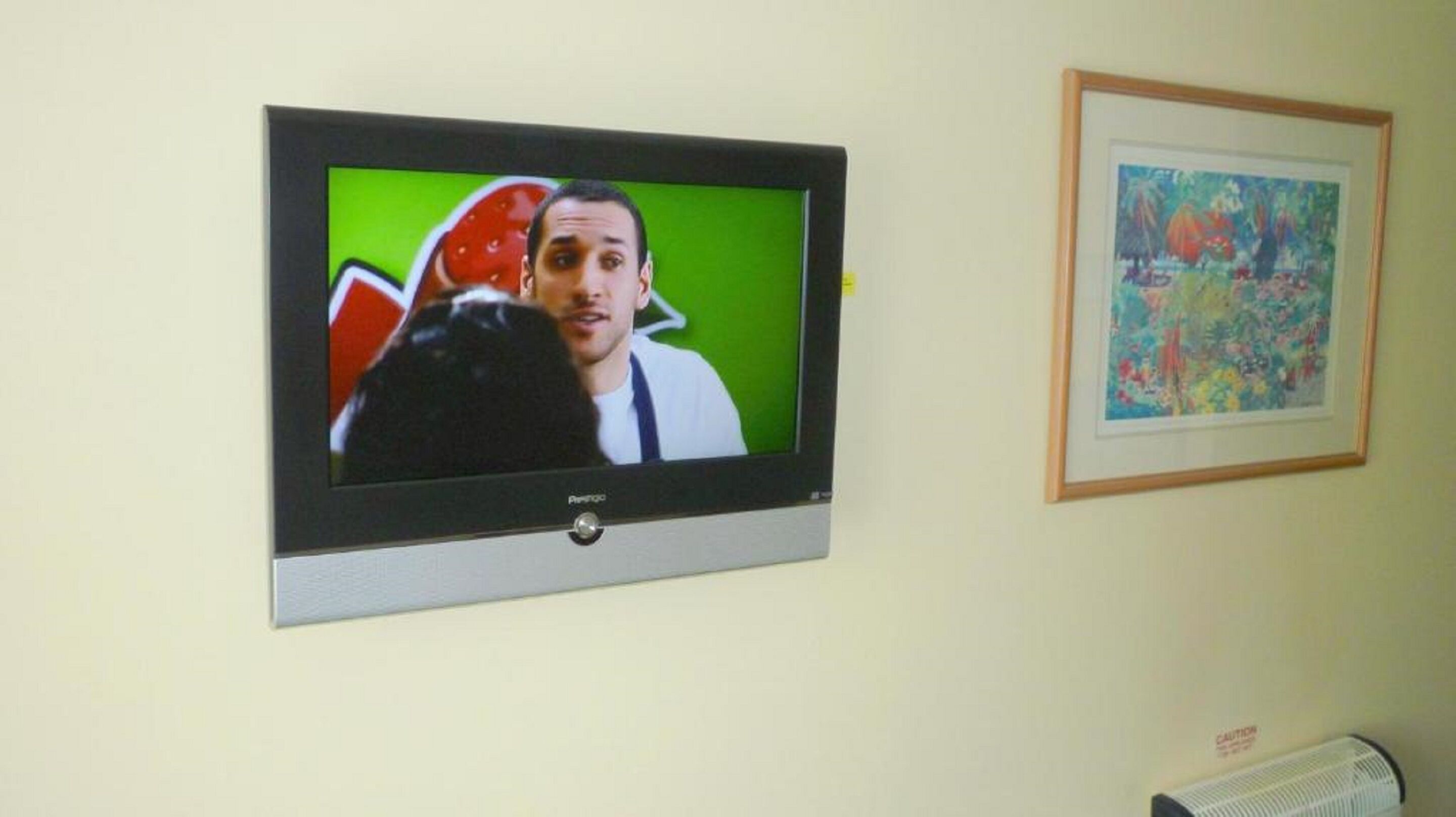 A television mounted on a wall with a framed painting beside it.