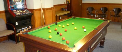 A pool table with balls, a dartboard, and a video game machine.