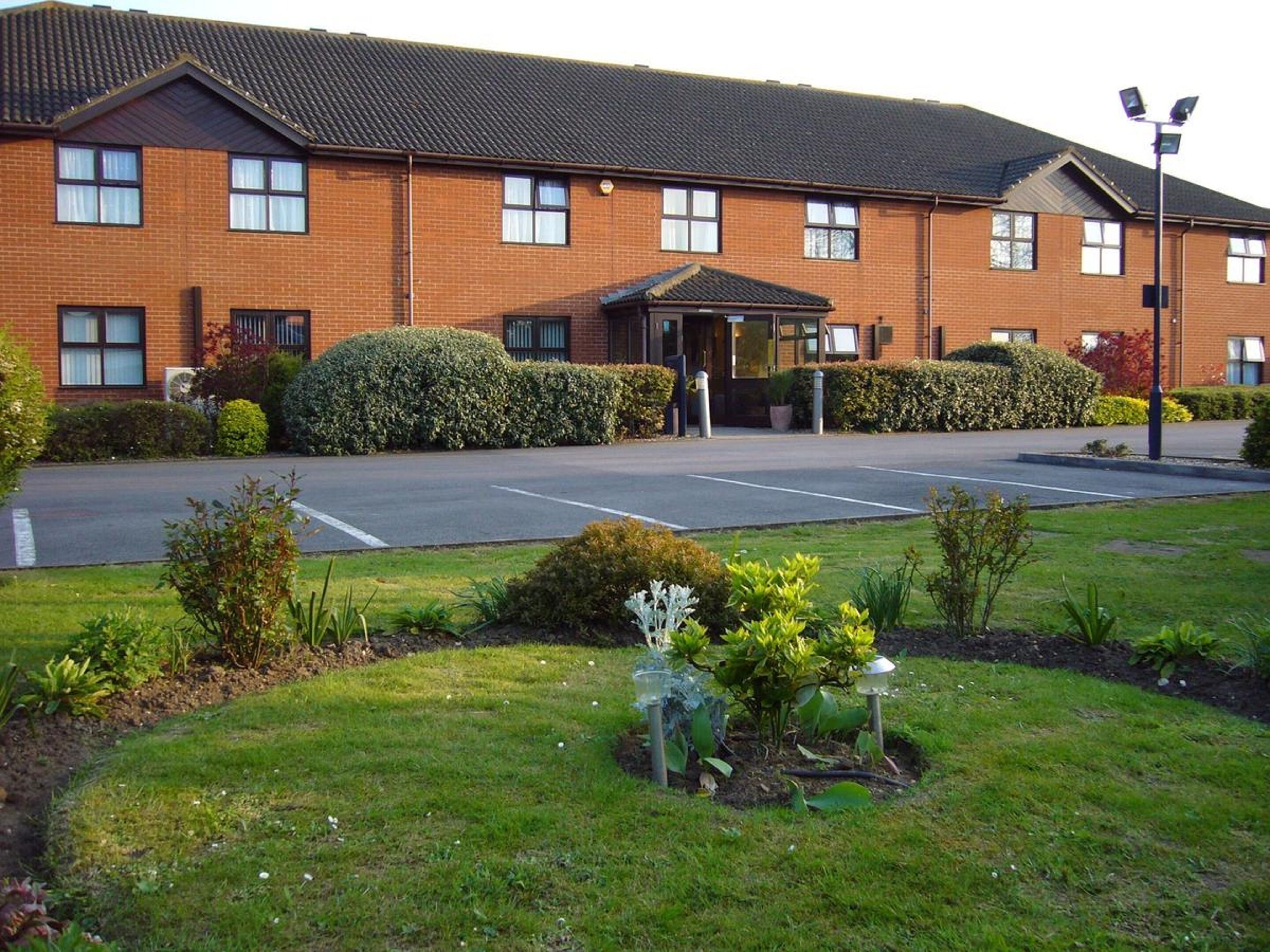 A brick building with a covered entrance, a parking lot, and well-maintained landscaping.