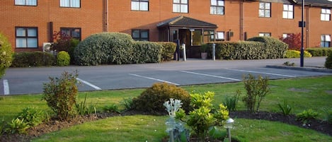 A brick building with a covered entrance, a parking lot, and well-maintained landscaping.