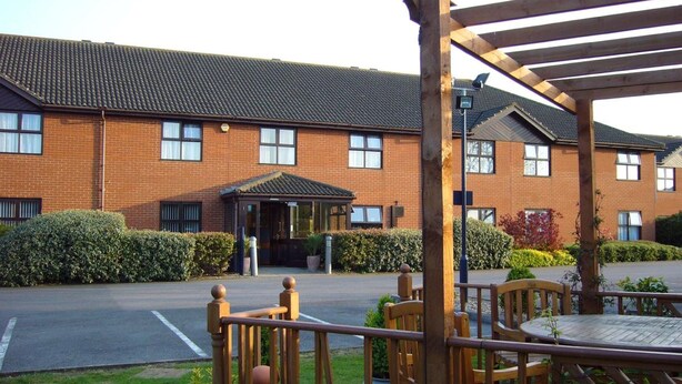 A brick building with a covered outdoor seating area and a paved driveway.