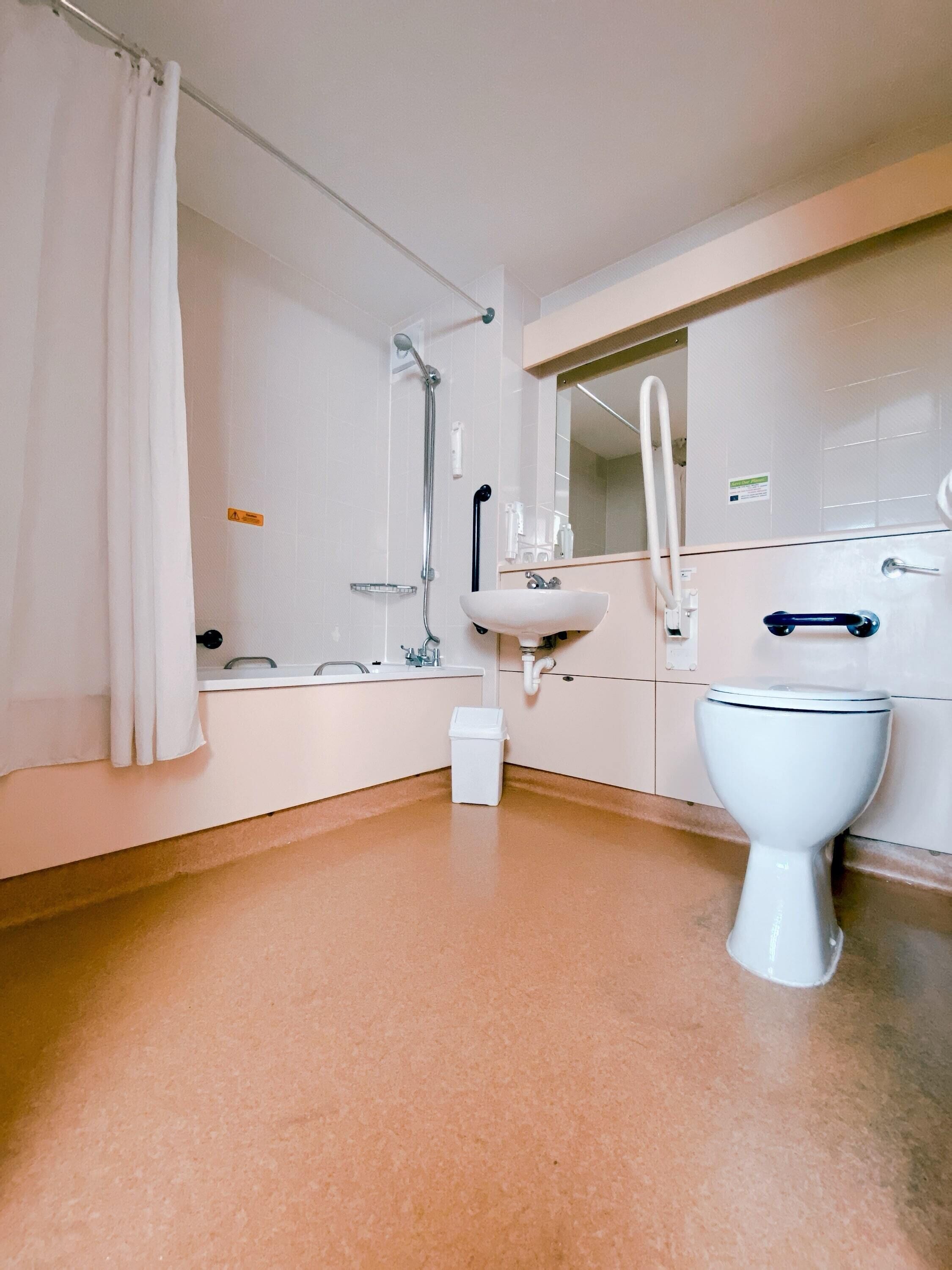 A bathroom with a white toilet, a sink, a shower, and a mirror.