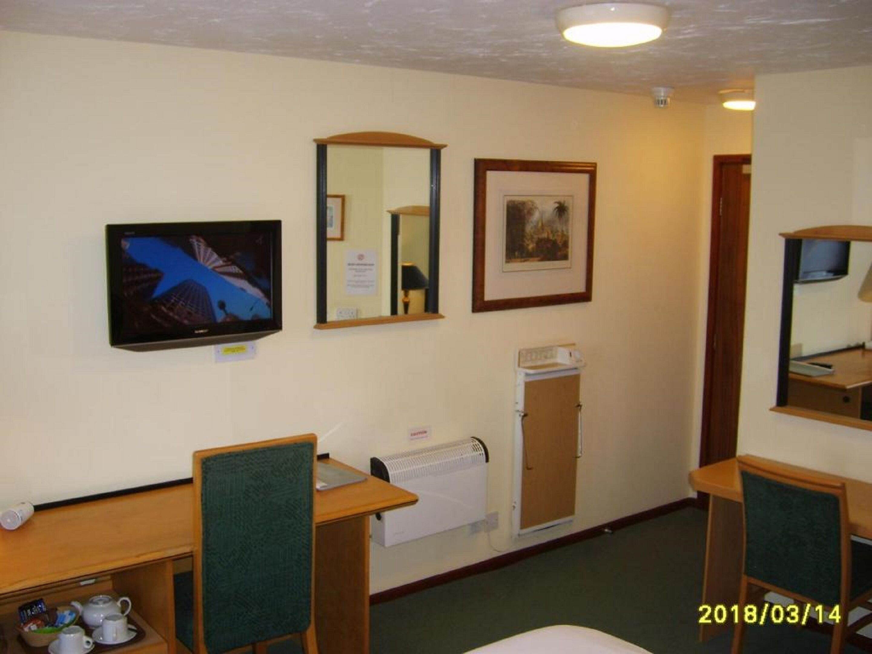 Una habitación de hotel con escritorio, dos sillas, televisor, radiador y un cuadro en la pared.