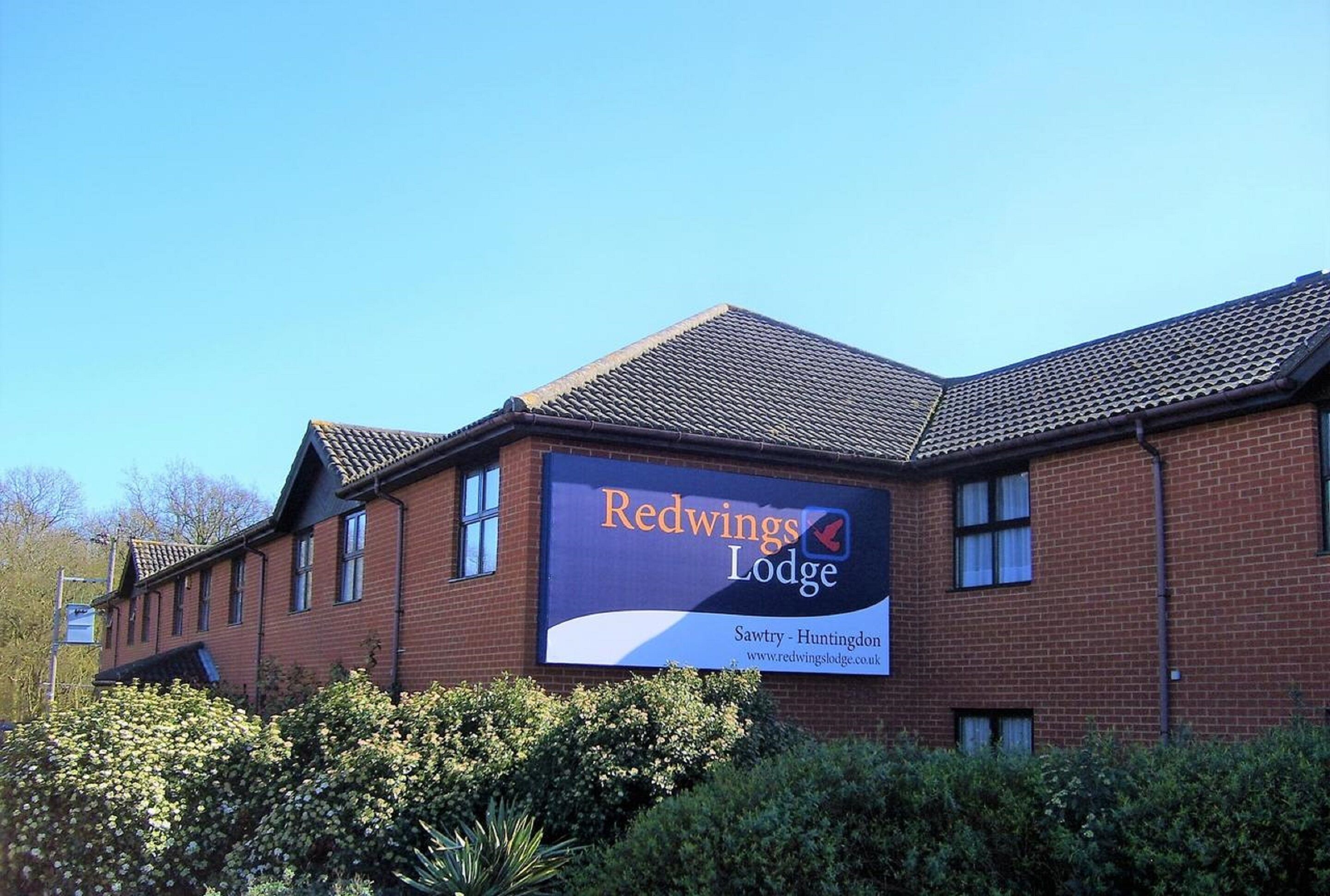 Een gebouw van Redwings Lodge met een groot bord waarop Sawtry - Huntingdon staat aangegeven.