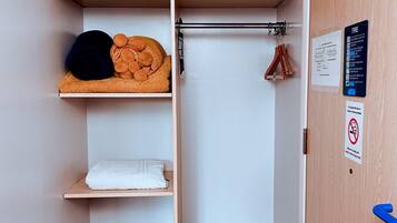 Un bagno compatto con portasciuga, mensole contenenti asciugamani e articoli da toilette, un piccolo cesto e una porta con cartelli di sicurezza.