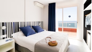 Una habitación de hotel con una cama, una mesita de noche, un ventanal con vista al mar y un balcón con barandilla.