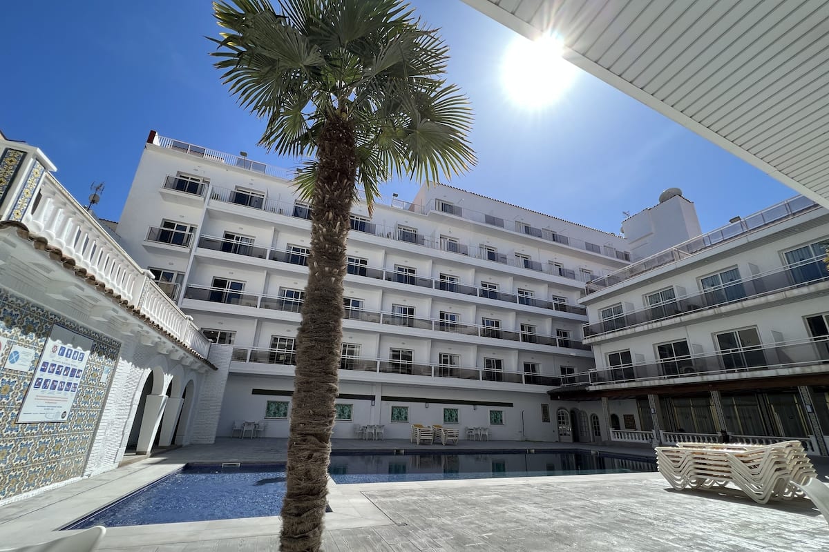 A multi-story hotel with balconies, a swimming pool, and a palm tree.