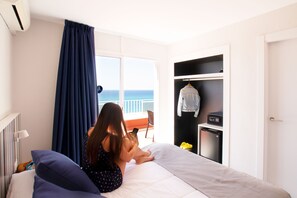 A bedroom with a bed, a window with a view of the sea, a wardrobe, and a small table with a chair. - Ibersol Hotel Sorra d'Or (Malgrat de Mar)