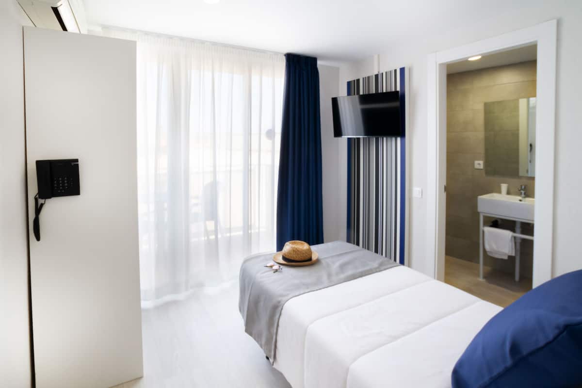 A hotel room with a bed, a TV mounted on the wall, a bathroom with a sink and mirror, and a door with a phone on the wall.