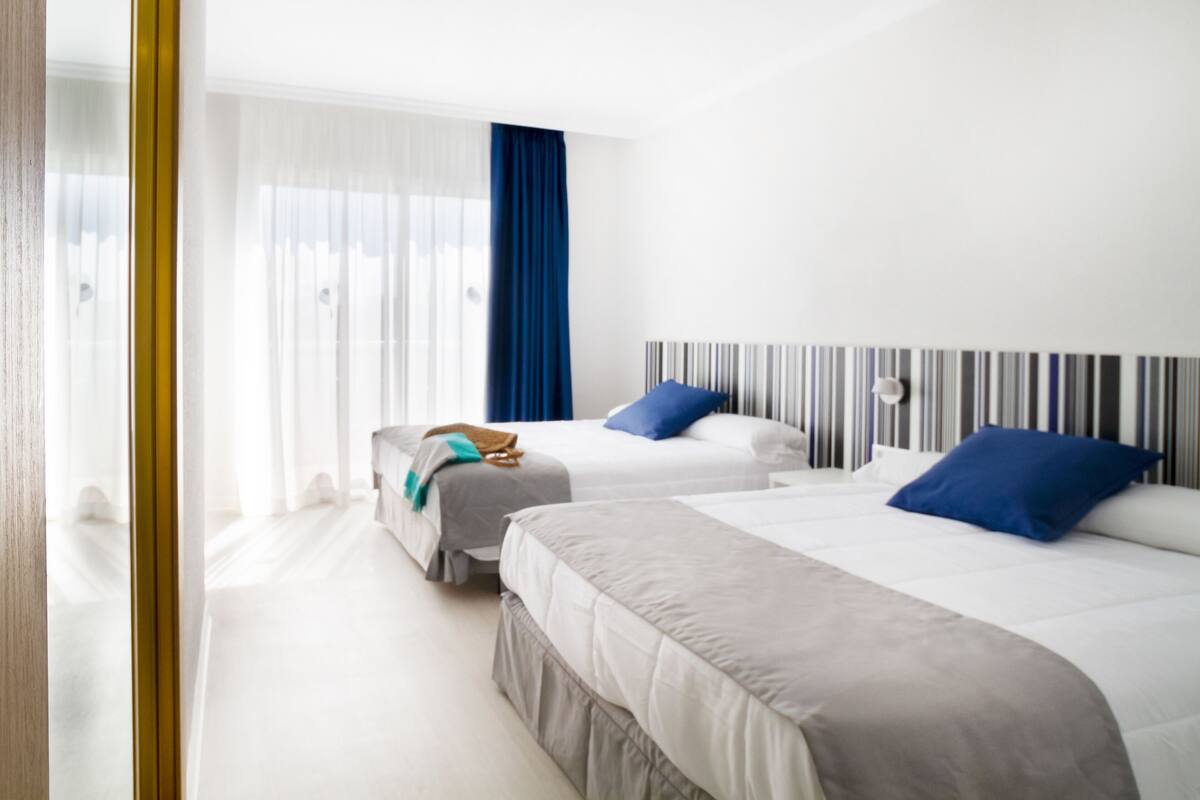 A hotel room with two beds, a striped headboard, and a large window with curtains.