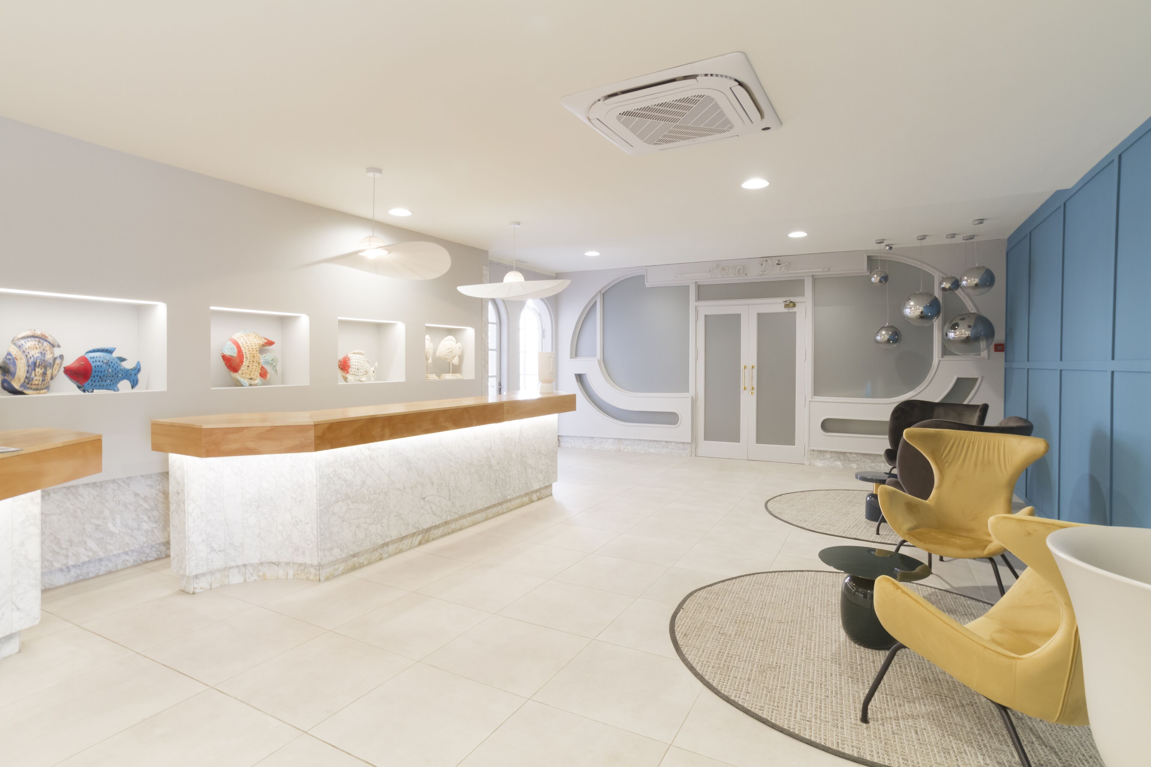 A reception area with a white reception desk, a seating area with yellow chairs, and a wall with abstract art.