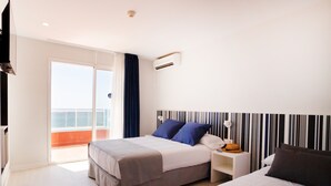 Un cuarto de hotel con cama, mesita de noche, lámpara y vista al exterior.