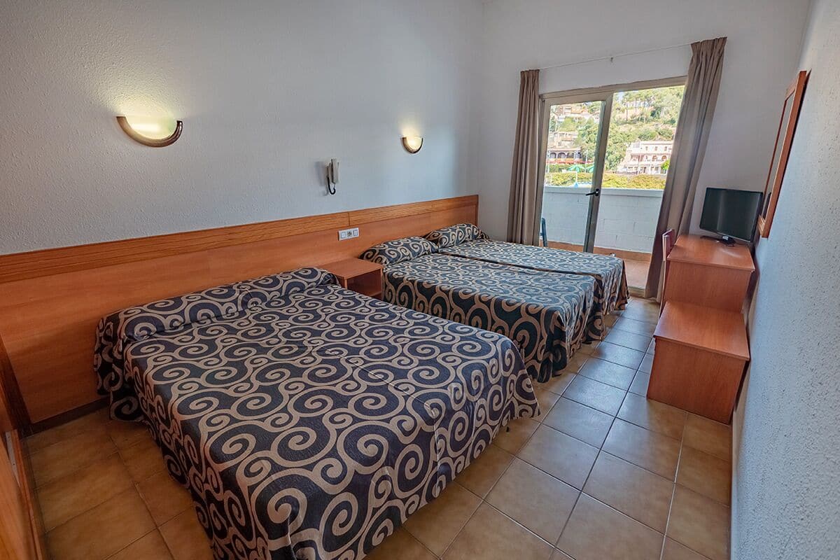 A hotel room with two beds, a desk, a TV, and a balcony with a view.