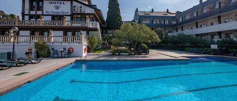 A hotel with a swimming pool, outdoor seating, and a large tree.