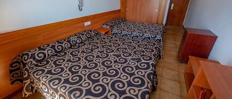 Habitación con tres camas, cabeceros de madera, teléfono junto a la cama y un armario de madera.