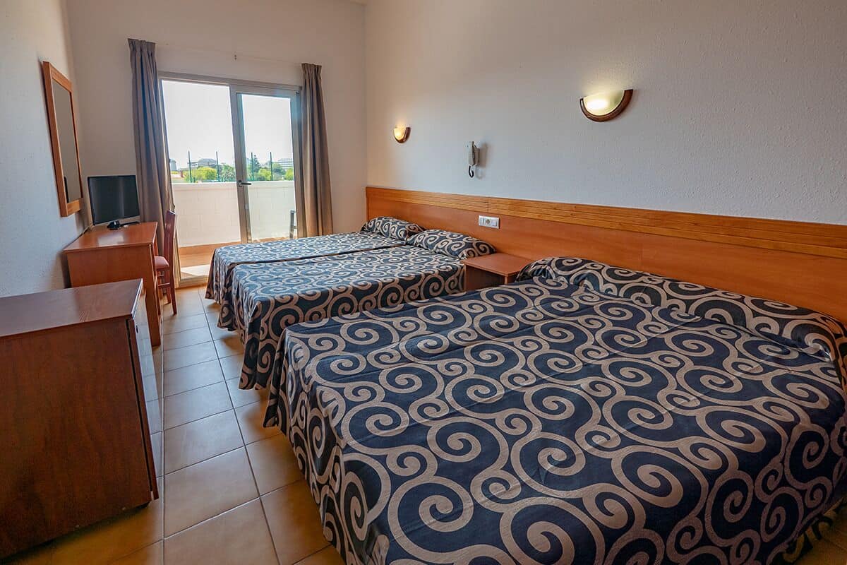 A hotel room with two beds, a desk, a chair, a television, and a sliding glass door to a balcony.
