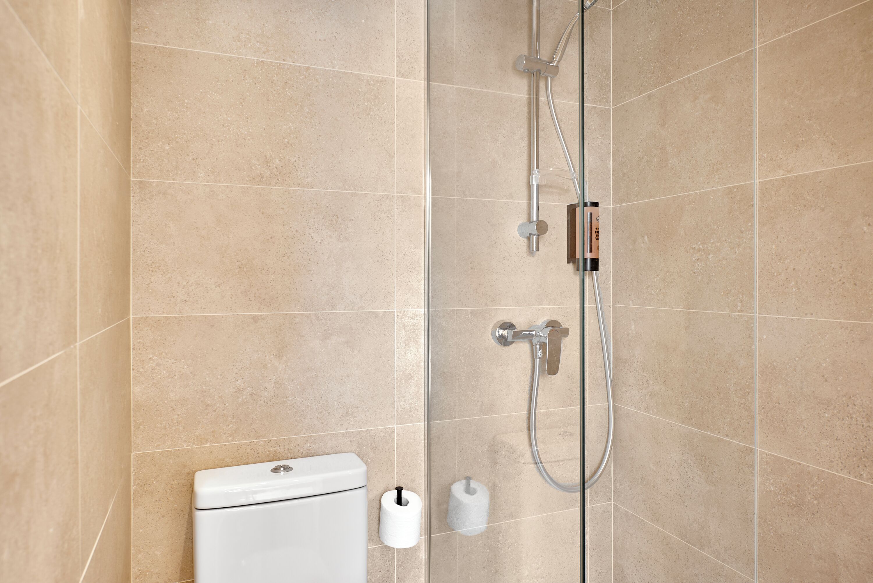 A modern bathroom with beige tiles, a toilet, and a shower with a handheld showerhead.