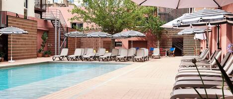 A pool area with lounge chairs and umbrellas, surrounded by buildings with balconies.