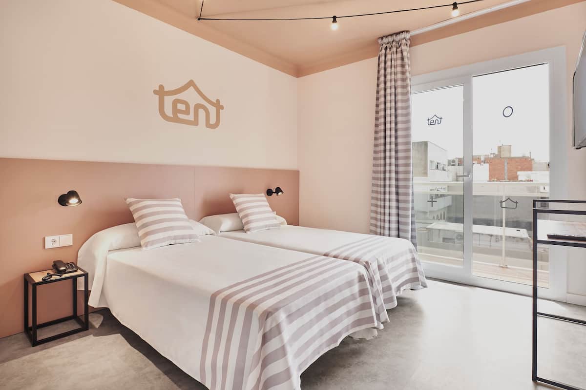 A hotel room with two beds, a nightstand with a phone, a wall-mounted light, and a large window with a curtain.