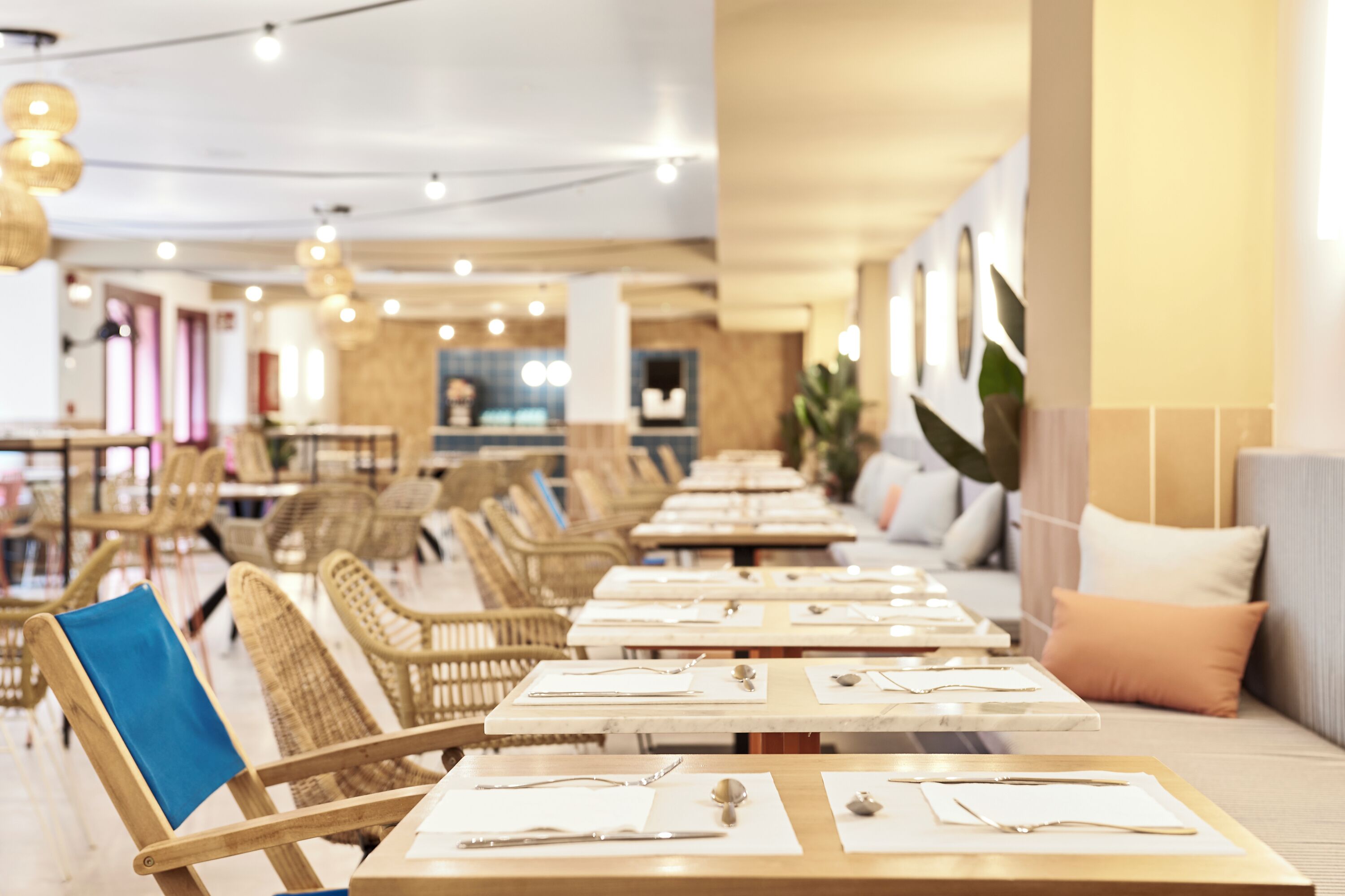 A restaurant with wooden tables and chairs, a bar area, and a seating area with cushions.