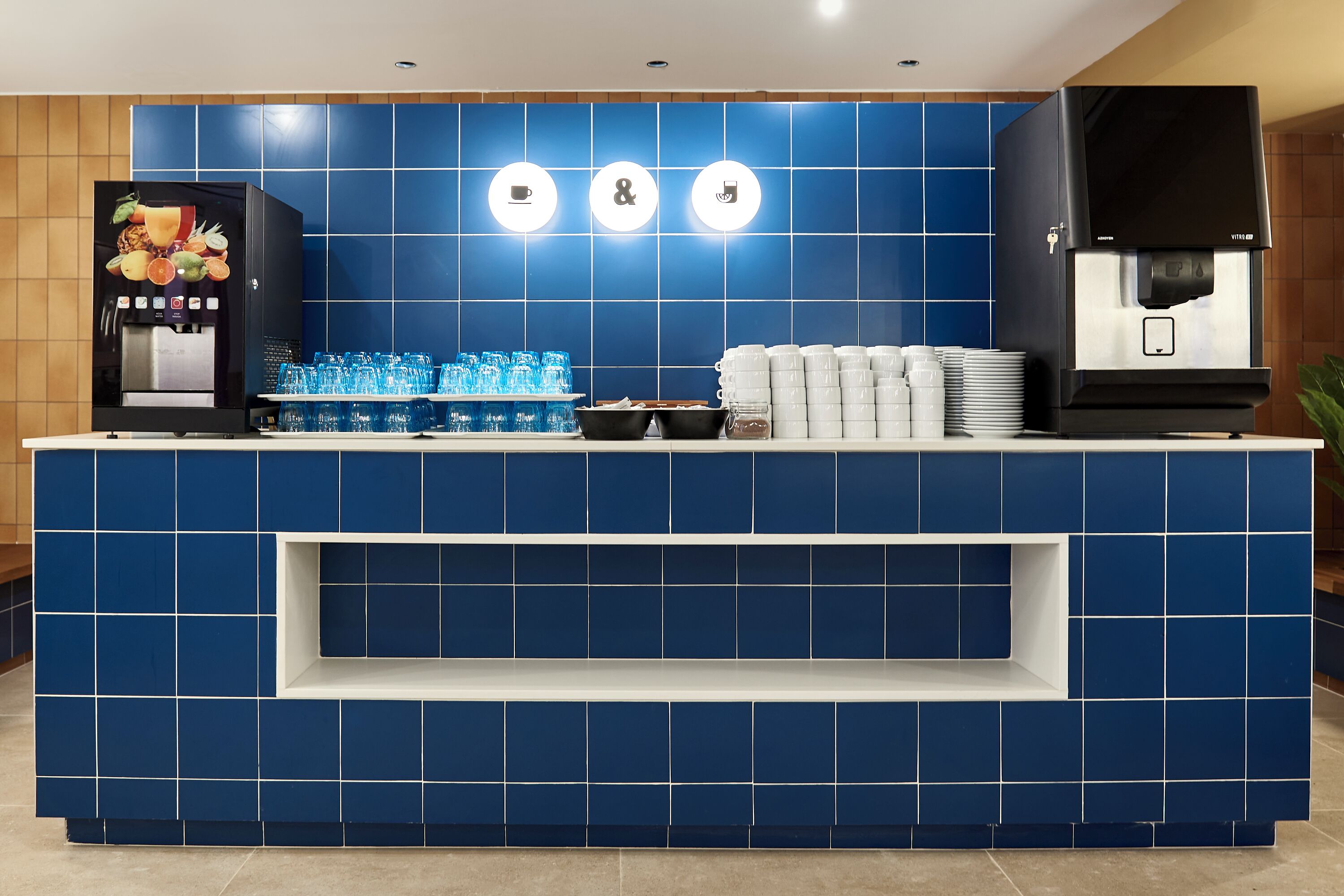 A blue-tiled reception desk with a coffee machine, glassware, and stacked plates.