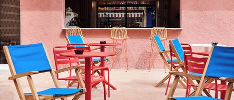 Een patio met rode en blauwe stoelen, een kleine ronde tafel en een raam met uitzicht op een bar.