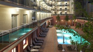 Un hotel de varios niveles con piscina, tumbonas y barandilla de cristal.