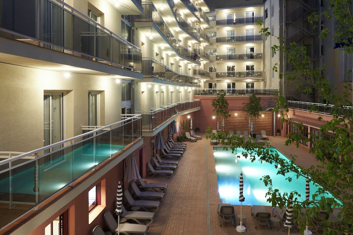 A multi-level hotel with a swimming pool, sun loungers, and a glass balustrade.