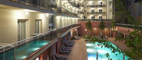Un hôtel à plusieurs étages doté d’une piscine, de chaises longues et d’une balustrade en verre.