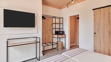 A bedroom with a bed, a TV mounted on the wall, a wooden wardrobe, and a small table with a basket.