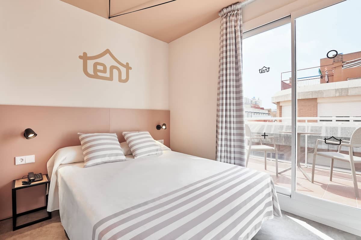 A hotel room with a bed, a nightstand, a phone, and a window with a view of the outside.